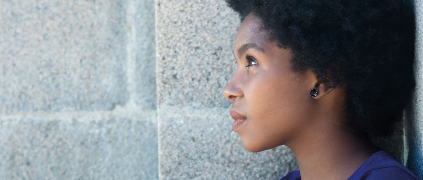 Eine afrikanisch aussehende Frau ist mit nachdenklichem Gesichtsausdruck an eine Wand gelehnt