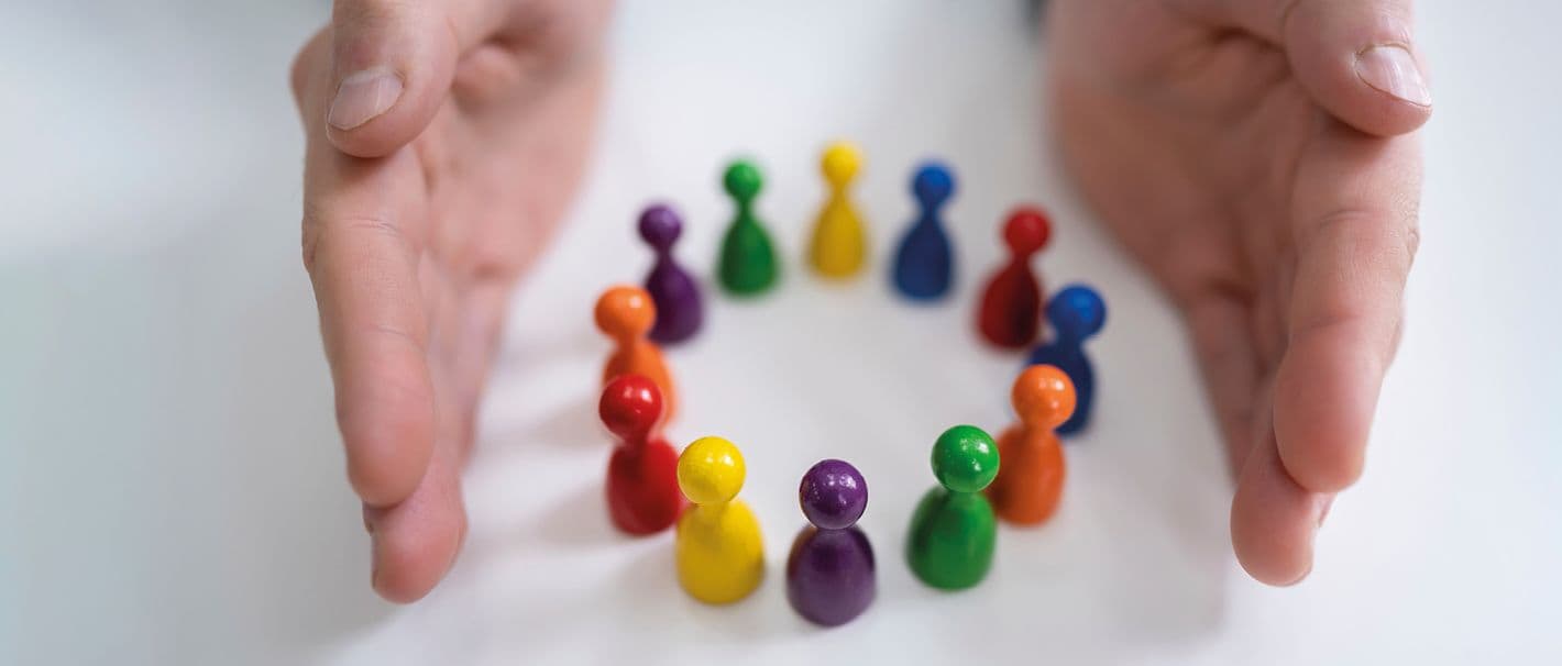 Spielfiguren in verschiedenen Farben sind in einem kleinen Kreis angeordnet. Zwei Handflächen befinden sich parallel zum Kreis und begrenzen ihn so nach außen.
