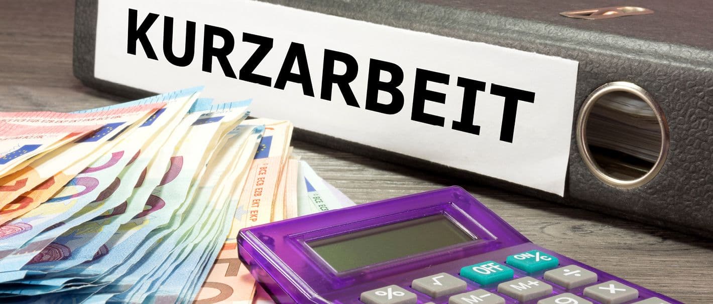 Aktenordner mit der Aufschrift „Kurzarbeit“. Daneben ein Taschenrechner und verschiedene Euroscheinen