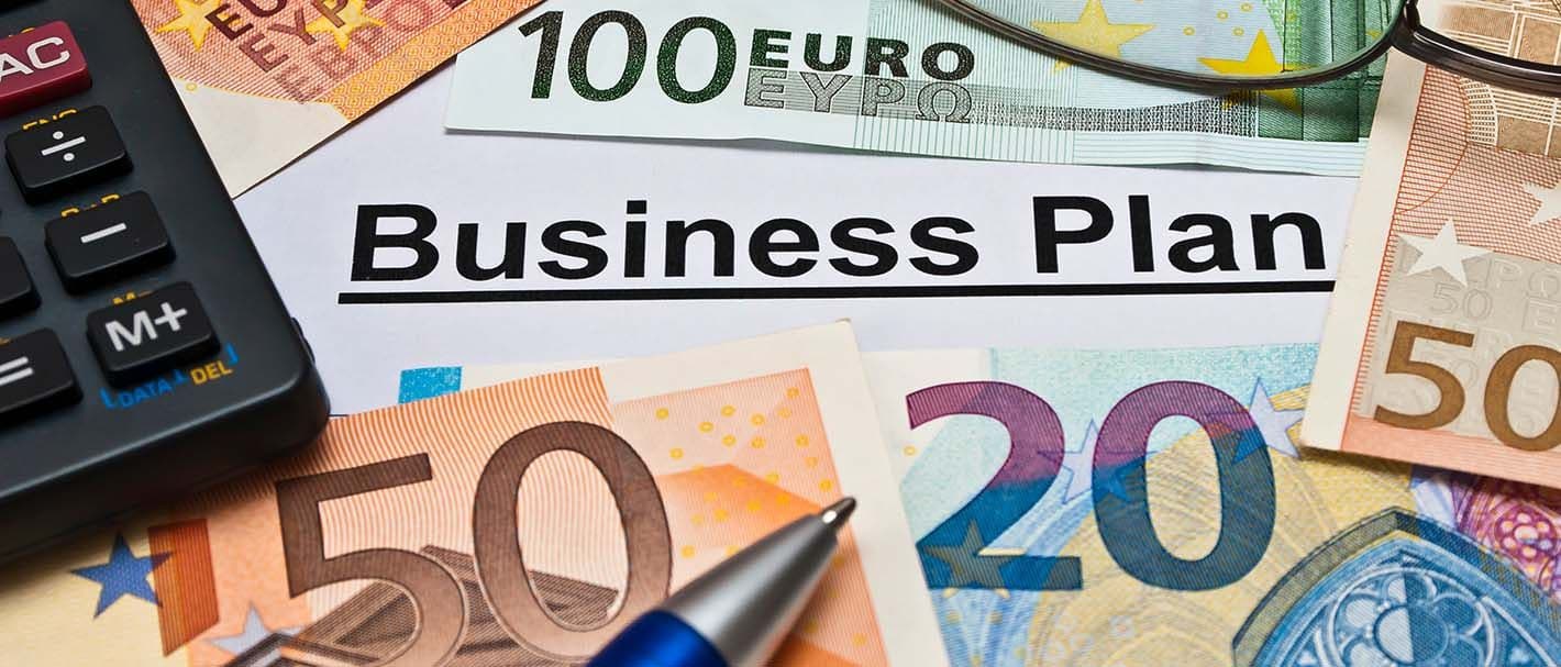 Nahaufnahme von einem Business-Plan, der größtenteils von Euro-Scheinen, einem Kugelschreiber, einer Brille und einem Taschenrechner verdeckt wird.