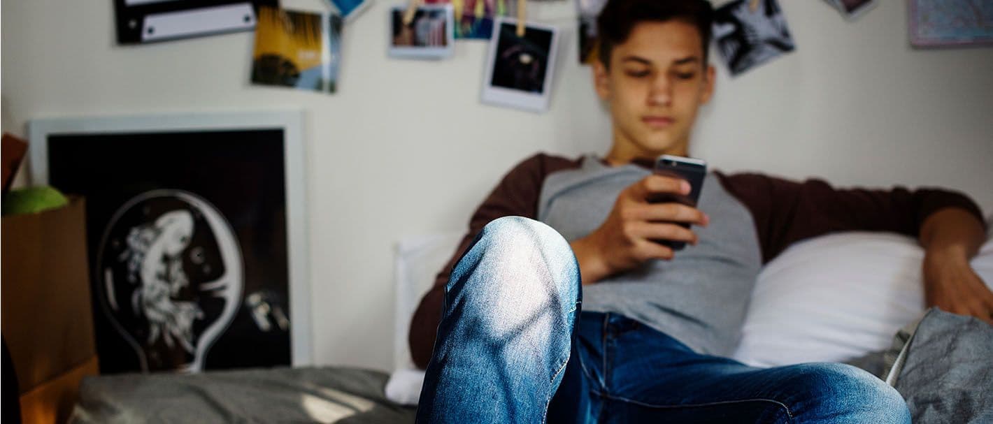 Jugendlicher sitzt mit seinem Smartphone auf seinem Bett.
