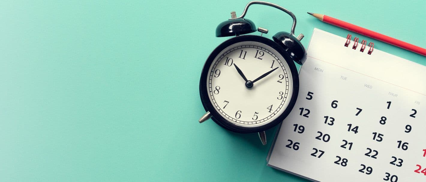 Wecker und Kalender und Bleistift auf türkisfarbenem Hintergrund.