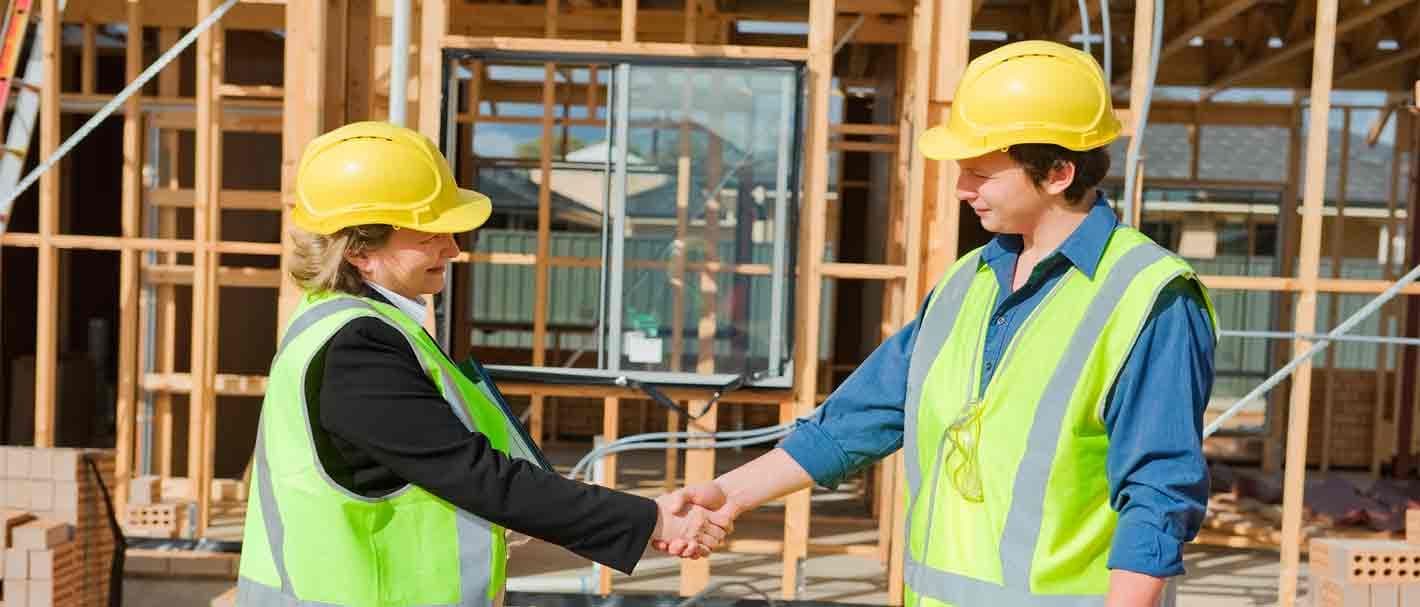 Zwei Frauen reichen sich auf einer Baustelle die Hand.