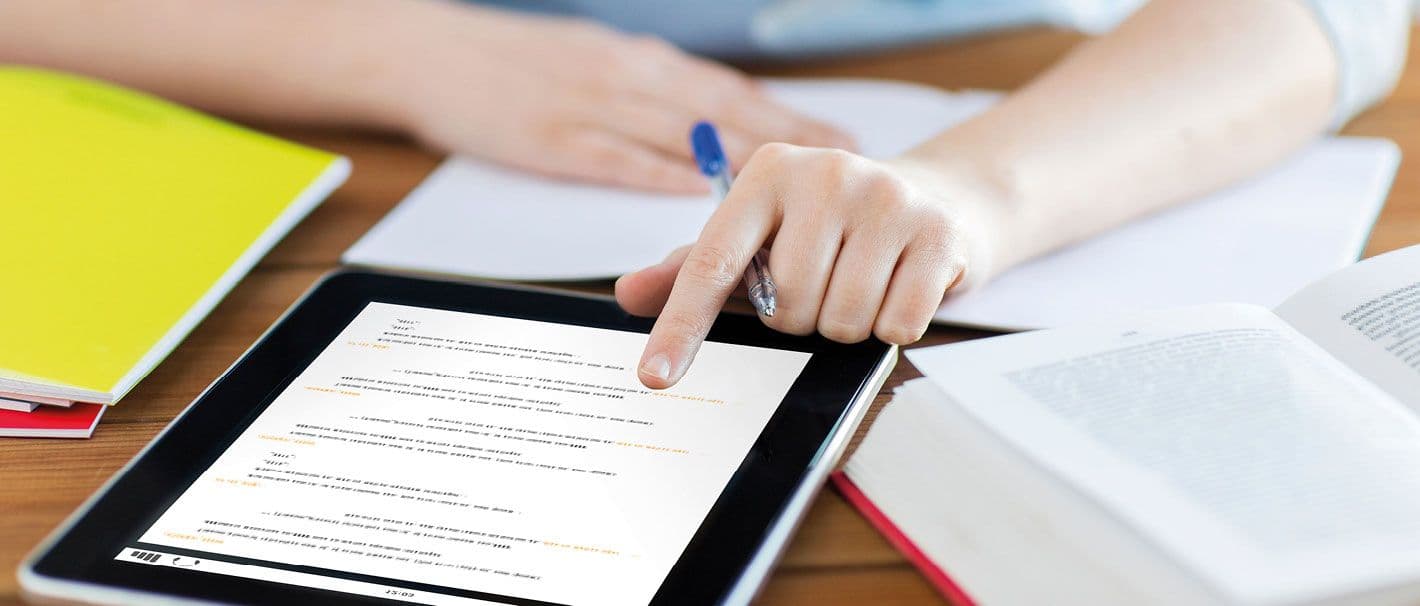 Bücher und Tablet auf einem Schreibtisch, an dem eine junge Frau sitzt