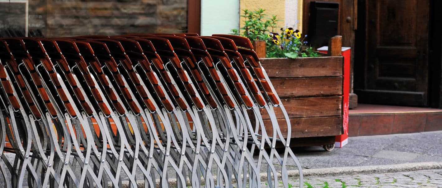 Zugeklappte Biergartenstühle in Reihe vor einem Haus mit offener Tür