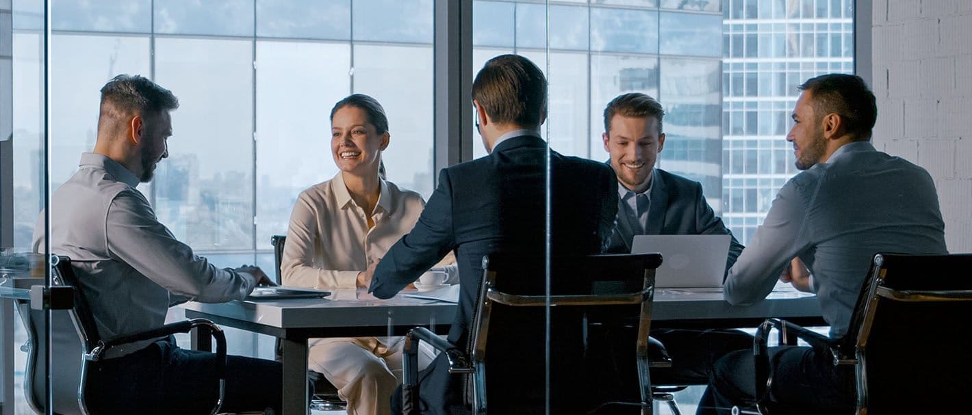 er Männer und eine Frau, alle in Businesskleidung, haben ein Meeting in einem hellen, modernen Besprechungsraum.