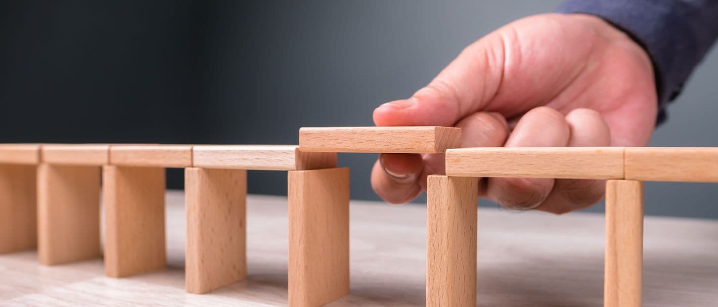 Hand, die eine Brücke aus Holzklötzen schließt, indem sie ein Verbindungsteil in die letzte Lücke zwischen den Pfeilern legt.
