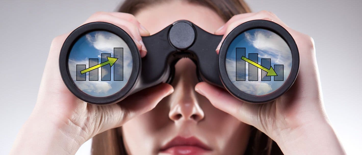 Eine Frau schaut durch ein Fernglas direkt in Richtung Betrachter. In beiden Gläsern spiegeln sich Wolken und transparent davor je ein Säulendiagramm mit aufsteigendem bzw. absteigenden Trend.