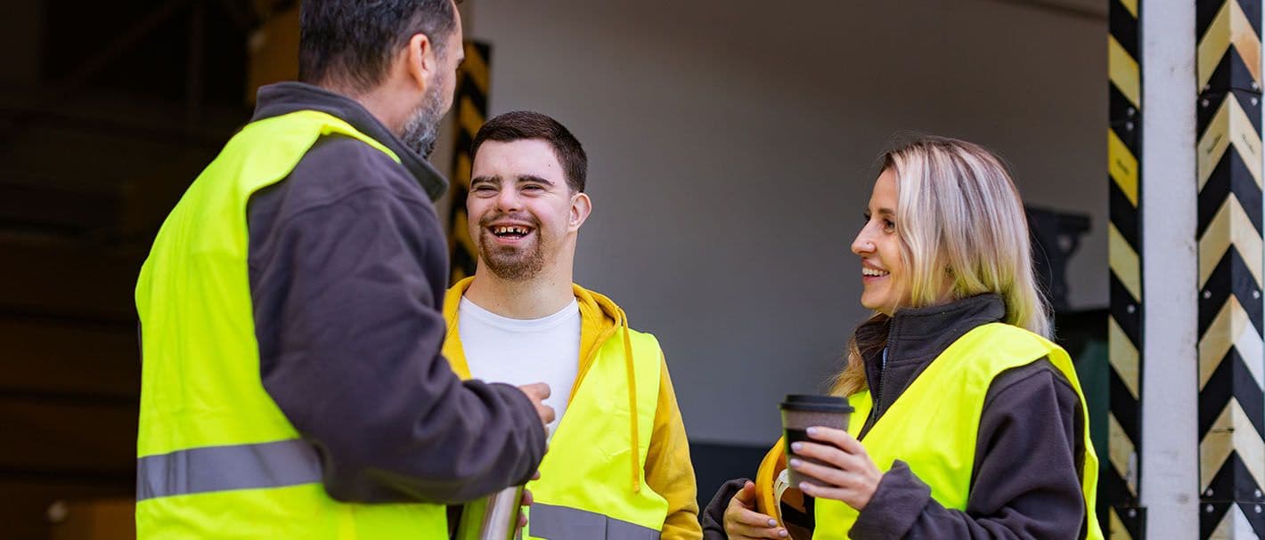 Ein Mann mit Down-Syndrom und seine Kollegen machen eine Arbeitspause und trinken Kaffee und heißen Tee draußen auf einer Laderampe.