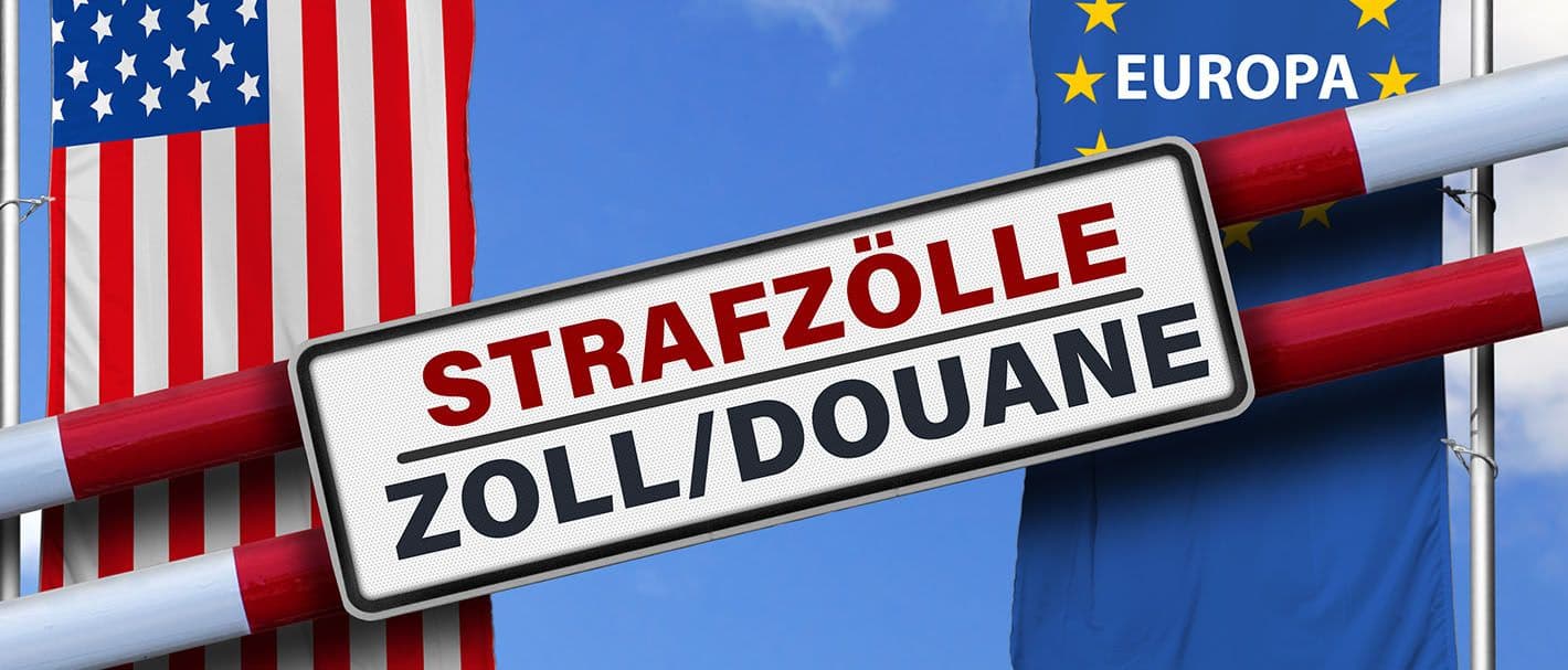 Zwei Schranken mit der Aufschrift „Strafzölle, Zoll Douane“ vor dem Hintergrund der Europäischen und der Amerikanischen Flagge.