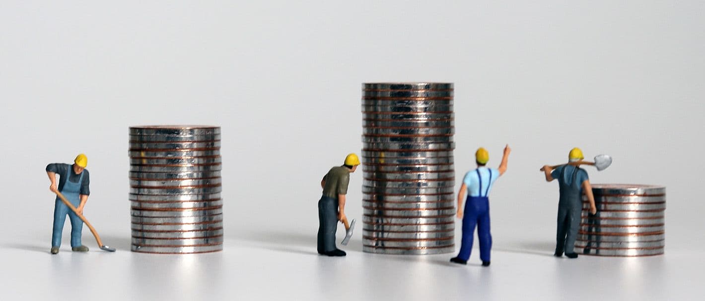 Bauarbeiter-Miniaturfiguren sind um Münzstapel arrangiert.