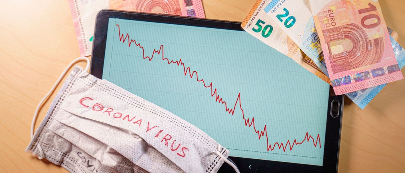 Geld, ein Tablet mit sinkendem Kurs auf dem Display und eine Atemschutzmaske liegen auf dem Tisch