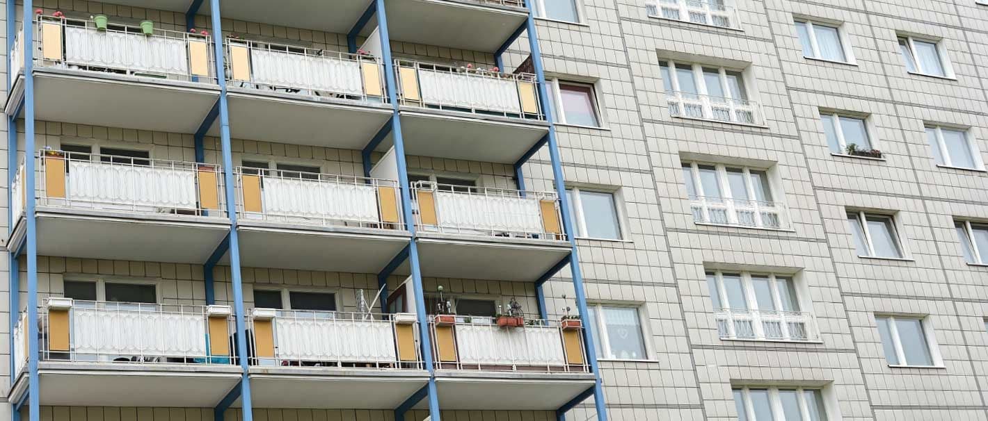 Trostlose Fassade eines Wohngebäudes. Die eine Hälfte der Wohnungen hat einen Balkon, die andere nicht.