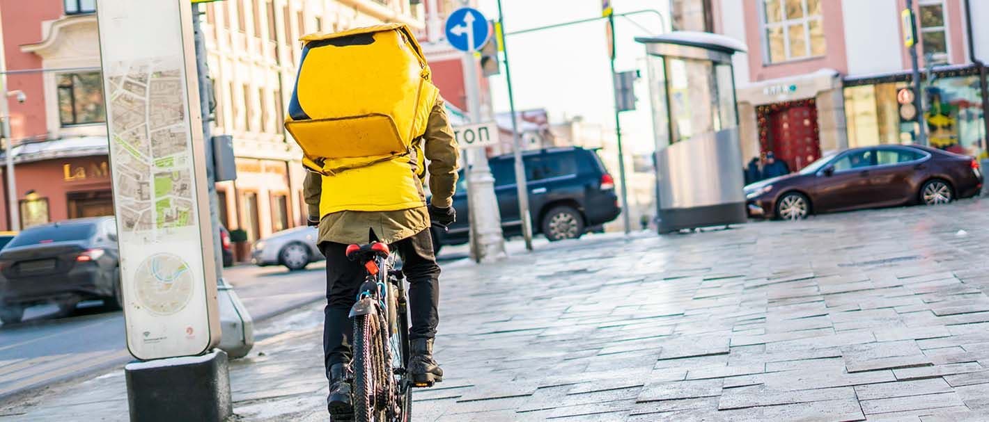 Rückansicht eines männlichen Fahrradkuriers mit einer gelben Transporttasche auf dem Rücken.